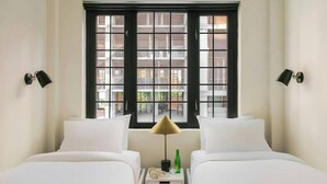A hotel room with two beds, a nightstand, a lamp, and a window with a view of buildings. - The Industrialist Belvilla District 6 Formerly Sonder (Brooklyn)