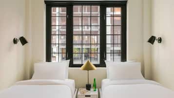 Quarto de hotel com duas camas, janela de moldura preta e abajur.