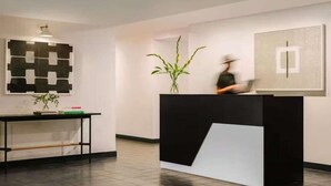 A reception area with a black and white desk, a potted plant, and a wall-mounted artwork. - The Industrialist Belvilla District 6 Formerly Sonder (Brooklyn)