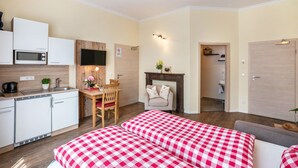 A compact hotel room with a kitchenette, a dining area, a fireplace, and a bed with checkered bedding. - Apartment 'Komfort  Römersberger - 4' with Wi-Fi (Vogtareuth)