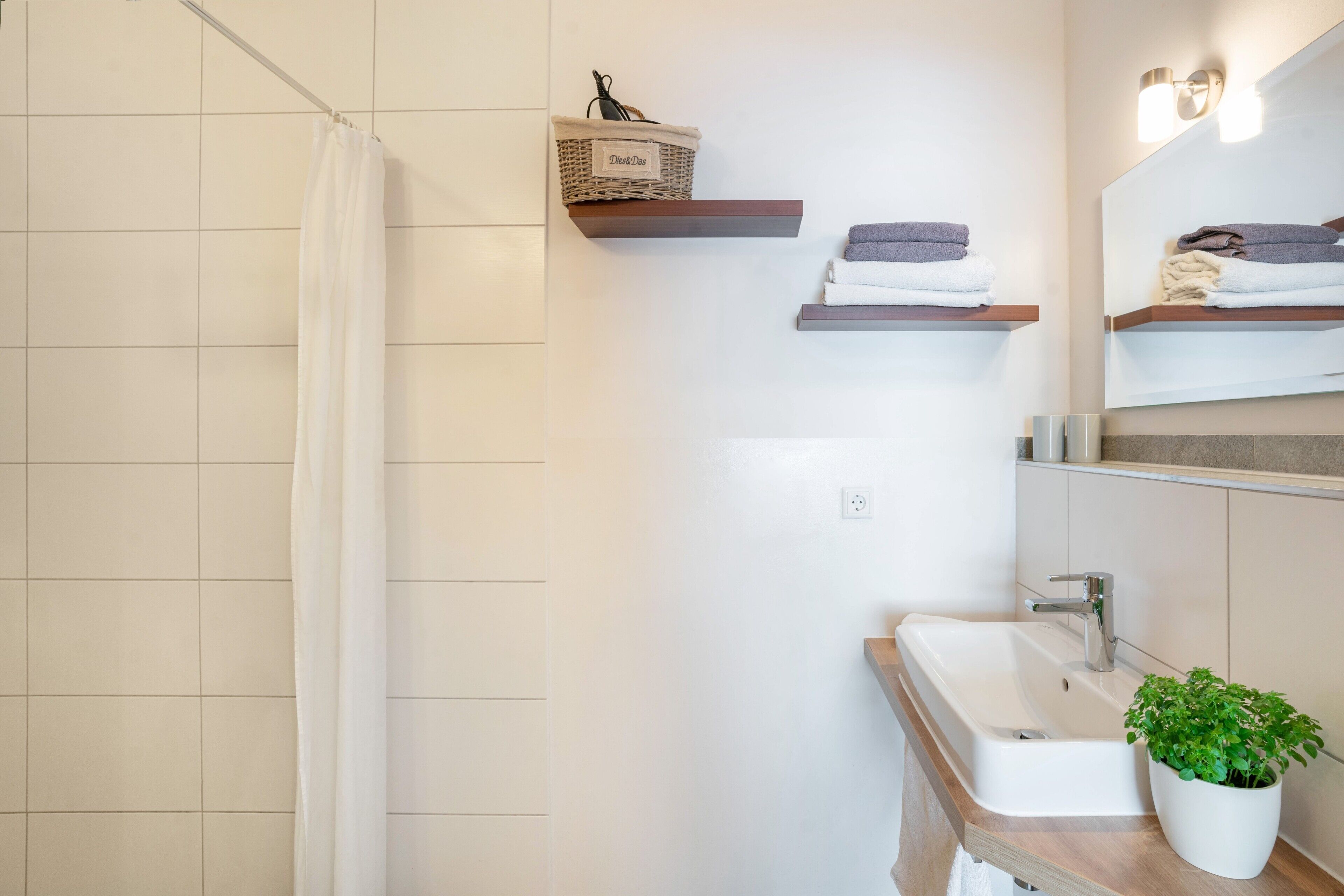 A bathroom with a shower curtain, a sink, a mirror, and shelves with towels.