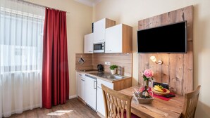 A compact kitchen with a microwave, sink, and wooden cabinets. A dining table with chairs and a vase of flowers is in the center. - Apartment 'Komfort  Römersberger - 4' with Wi-Fi (Vogtareuth)