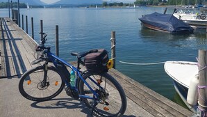A wooden dock with a bicycle and a bag, a boat docked at the pier, and a calm lake with sailboats and mountains in the background. - Holiday Apartment 'Komfort Römersberger - 6' with Private Terrace, Private Garden and Wi-Fi (Vogtareuth)