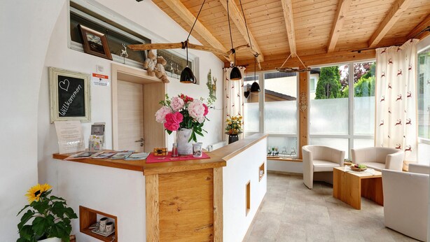 A modern interior with a wooden reception desk, a seating area with white sofas, and a large window with curtains. - Holiday Apartment 'Komfort Römersberger - 6' with Private Terrace, Private Garden and Wi-Fi (Vogtareuth)
