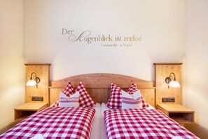 Cama doble con ropa de cama a cuadros, cabecera de madera, lámparas de noche y una pared con una cita.