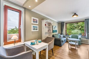 Una habitación con una mesa de comedor, sillas, un sofá, una mesita y una ventana con cortinas.