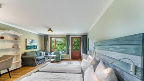 Habitación de hotel con dos camas, un sofá, una silla, una mesita y una estantería.