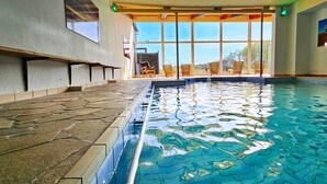 Una piscina interior con agua cristalina, suelo de piedra y sillas de madera.