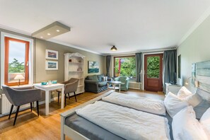 A hotel room with a bed, a desk, a chair, a sofa, and a view of greenery outside.