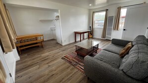 A modern living room with a grey sofa, a wooden bench, a glass coffee table, and a patterned rug. - Updated 1BR w/ Kitchen, Fast WiFi + Highway Access Near Carrizo Plain (Cuyama)