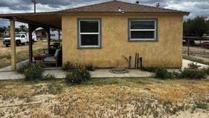 A small single-story house with a covered porch, two windows, and a hose on the ground. - Updated 1BR w/ Kitchen, Fast WiFi + Highway Access Near Carrizo Plain (Cuyama)