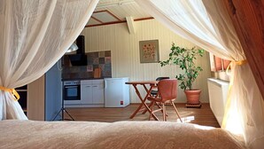 Una habitación acogedora con cama, una mesa, sillas, una planta en maceta, una zona de cocina con armarios y electrodomésticos, y un techo con vigas de madera.