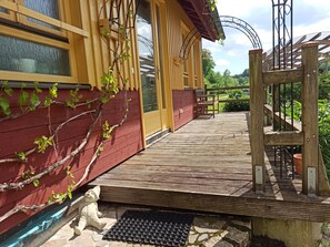 Une terrasse en bois avec un banc, une petite statue de jardin et une rambarde en métal.