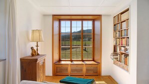 Una habitación con un ventanal grande, un banco de madera, una estantería y una lámpara.
