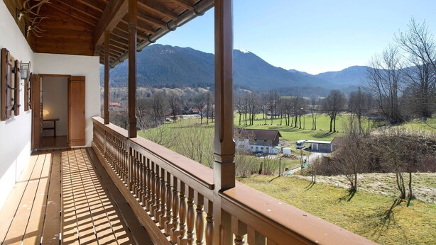 Un balcón de madera con vistas a montañas y un paisaje rural.