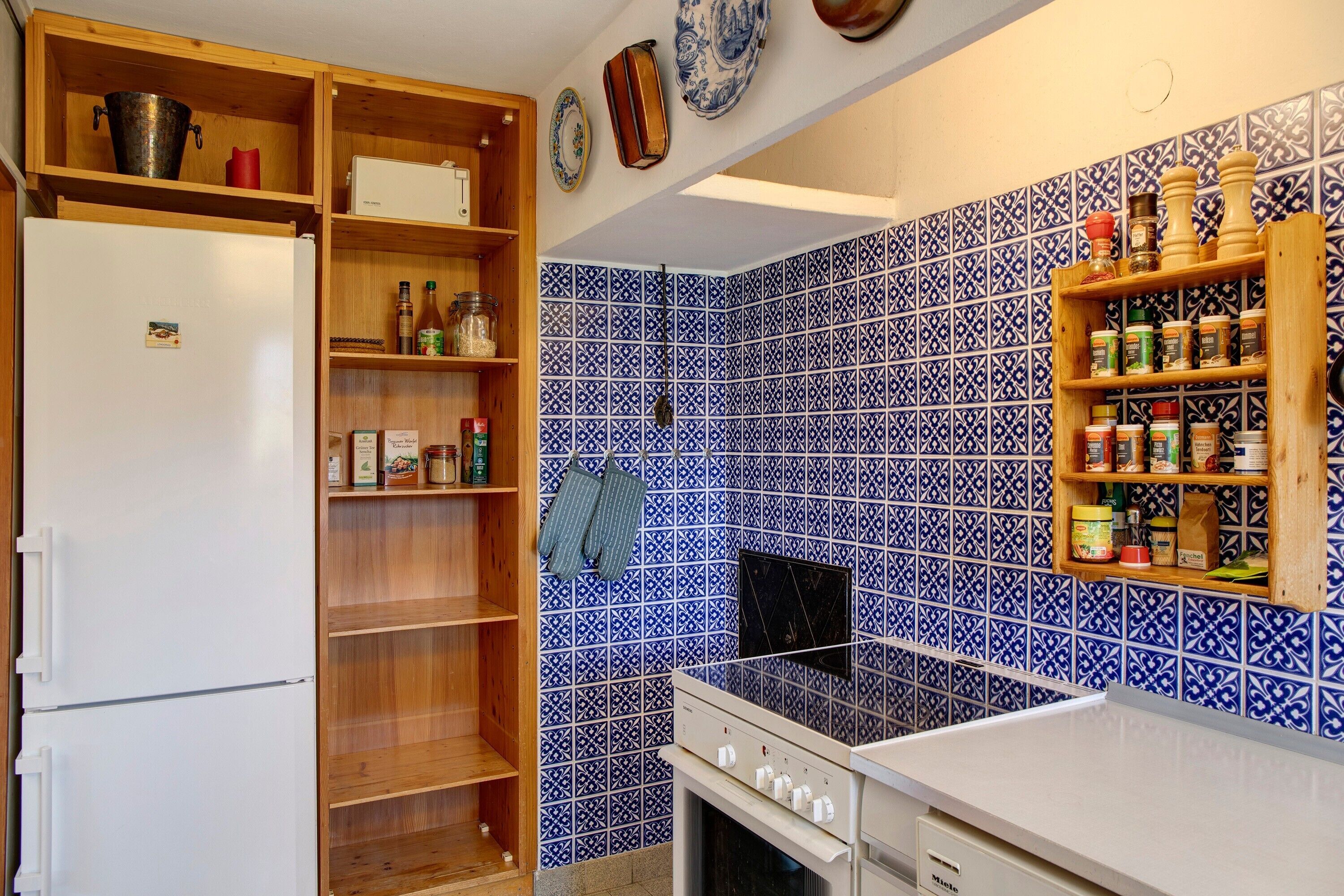 A kitchen with a white refrigerator, wooden shelves, a stove, and blue patterned tiles.