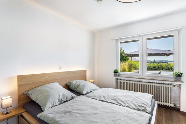 A bedroom with a bed, bedside table, lamp, window with view, and radiator.