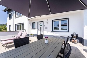 A patio with a table, chairs, a grill, and a covered area with umbrellas. - Panoramanest Sauerland with Sun Terrace, Quiet Location, Near Sorpesee, Hiking Trails (Balve)