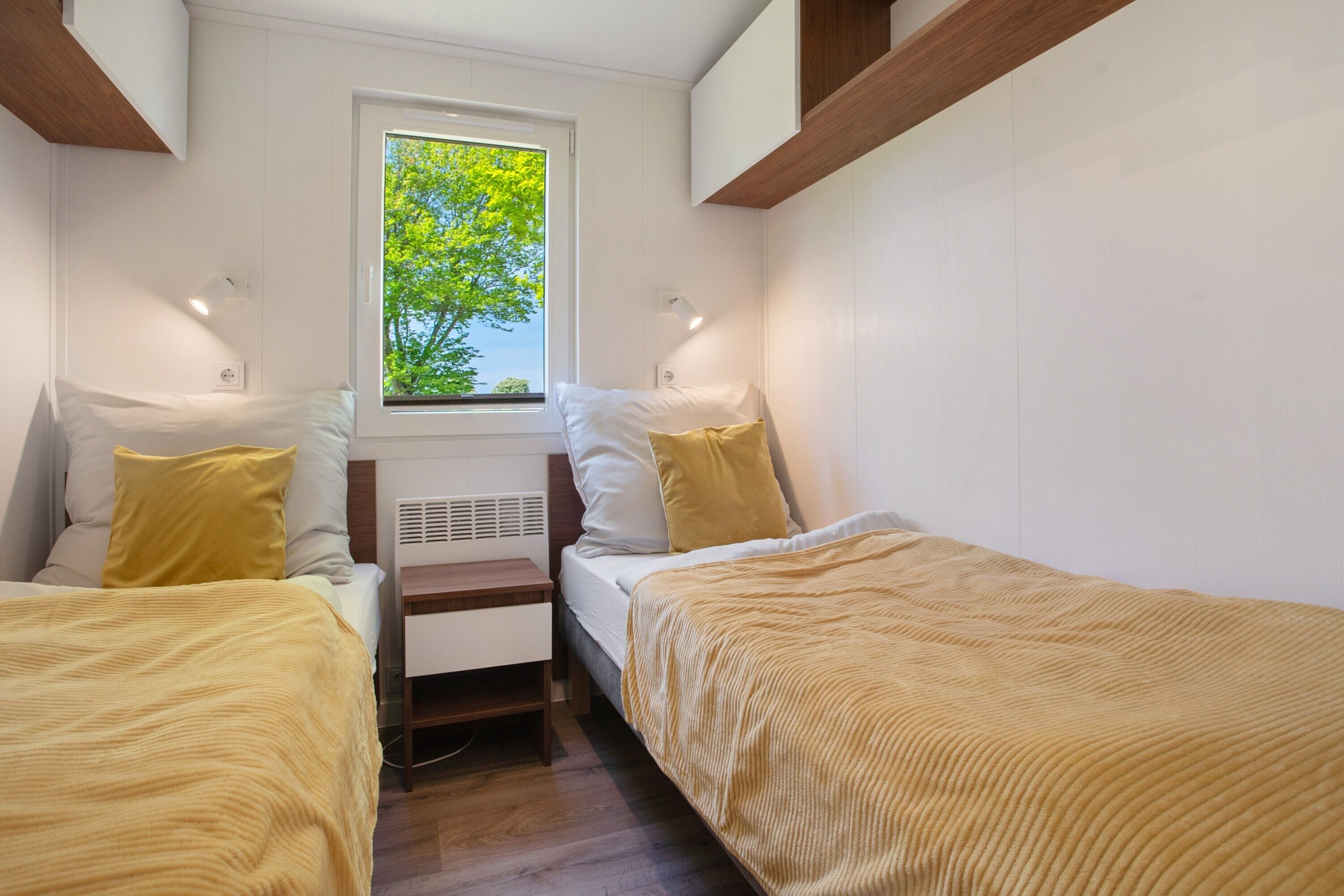 A small, well-lit bedroom with two beds, a window, and a nightstand.
