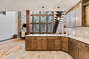 A spacious kitchen with a large island, wooden cabinets, and a stone accent wall. - Hidden Bear | Hot Tub, Game Room & Near Yellowstone! (Ashton)
