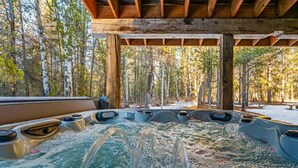Ein Bereich mit mehreren Whirlpools unter einer Holzkonstruktion, umgeben von bewaldetem Gelände mit Schnee.