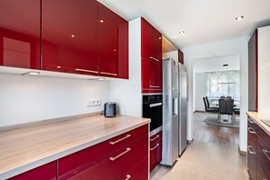 A modern kitchen with red cabinets, stainless steel appliances, and a wooden countertop. - Apartment 'Zum Alten Wald' with Private Terrace and Wi-Fi (Zell am Harmersbach)