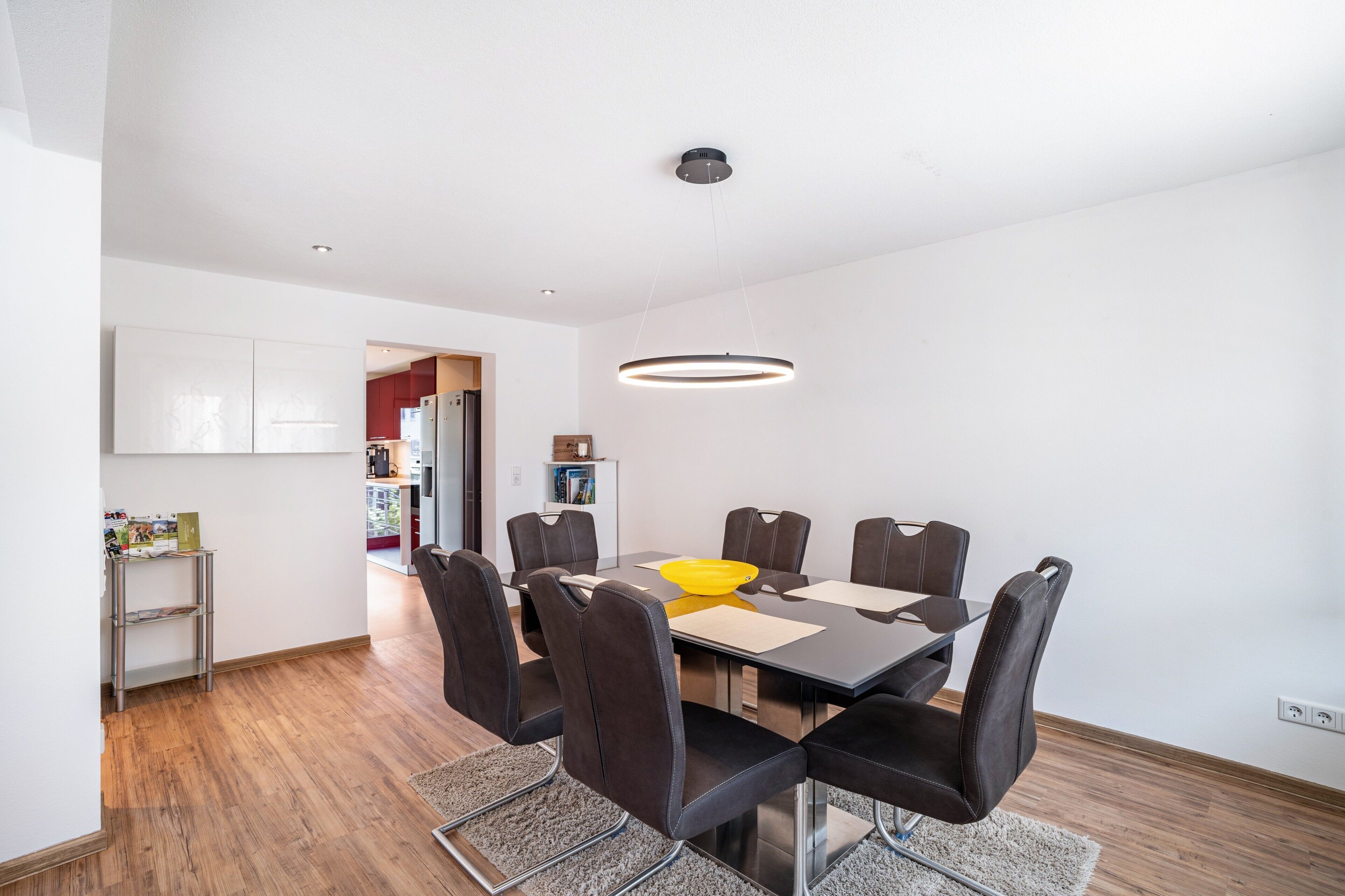A modern dining area with a round table, chairs, and a pendant light.