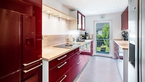 A modern kitchen with red cabinets, a wooden countertop, and a view of the outdoors through a glass door.