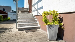 A set of outdoor stairs leading to a building entrance, a concrete planter with a small tree, and a metal handrail.