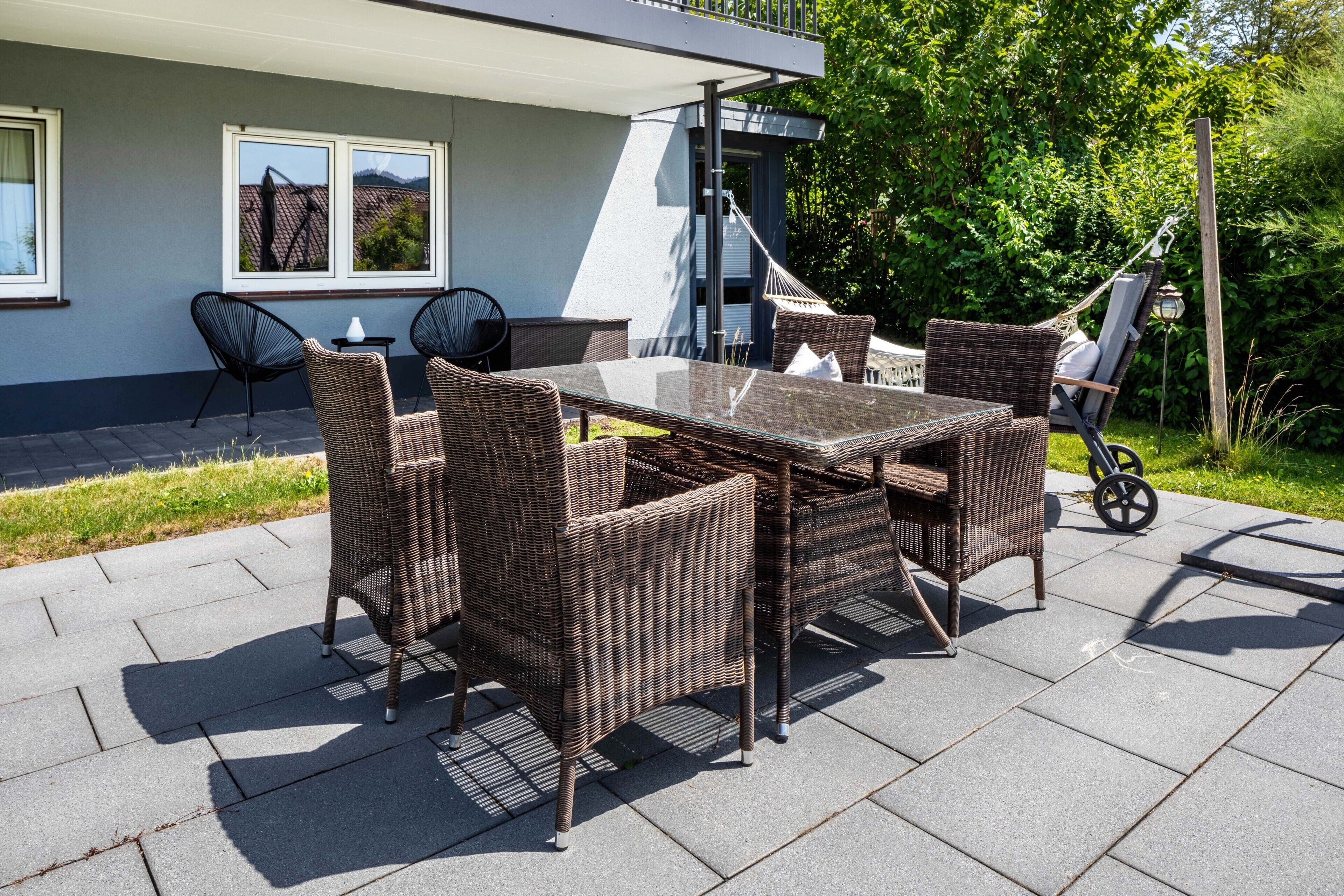 Eine Terrasse im Freien mit Korbmöbeln, einem Glastisch und Blick auf das Haus.