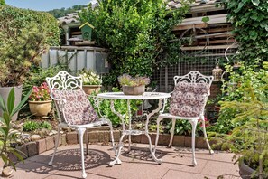 Een terras met twee witte metalen stoelen en een kleine ronde tafel, omringd door potplanten en een tuin.