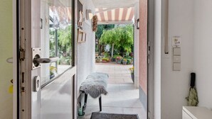 Una puerta abierta que da a un balcón con un toldo a rayas, un pequeño banco y plantas en macetas.