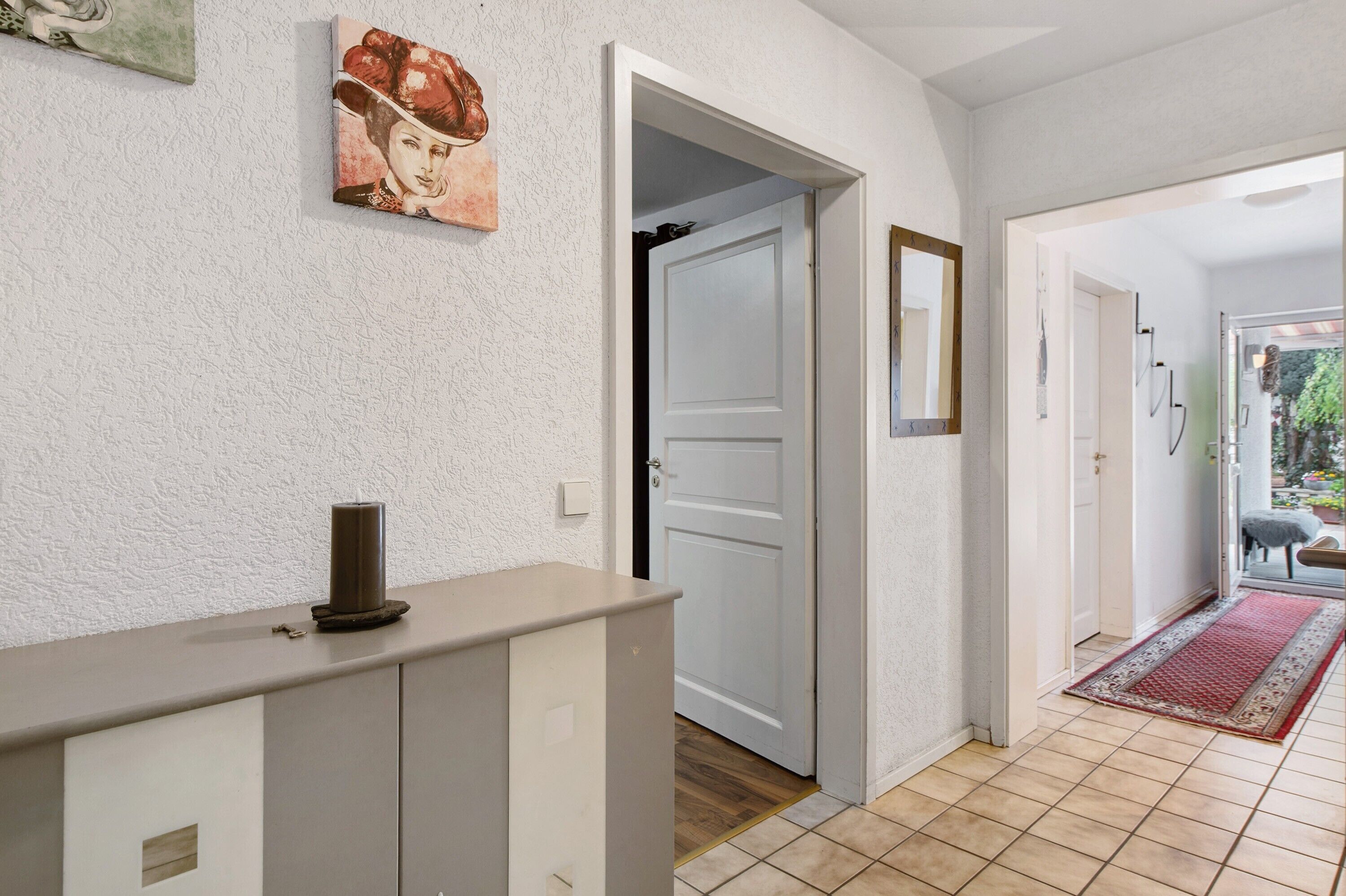 Un pasillo con una puerta blanca, un mostrador color crema y una alfombra roja que conduce a un jardín.