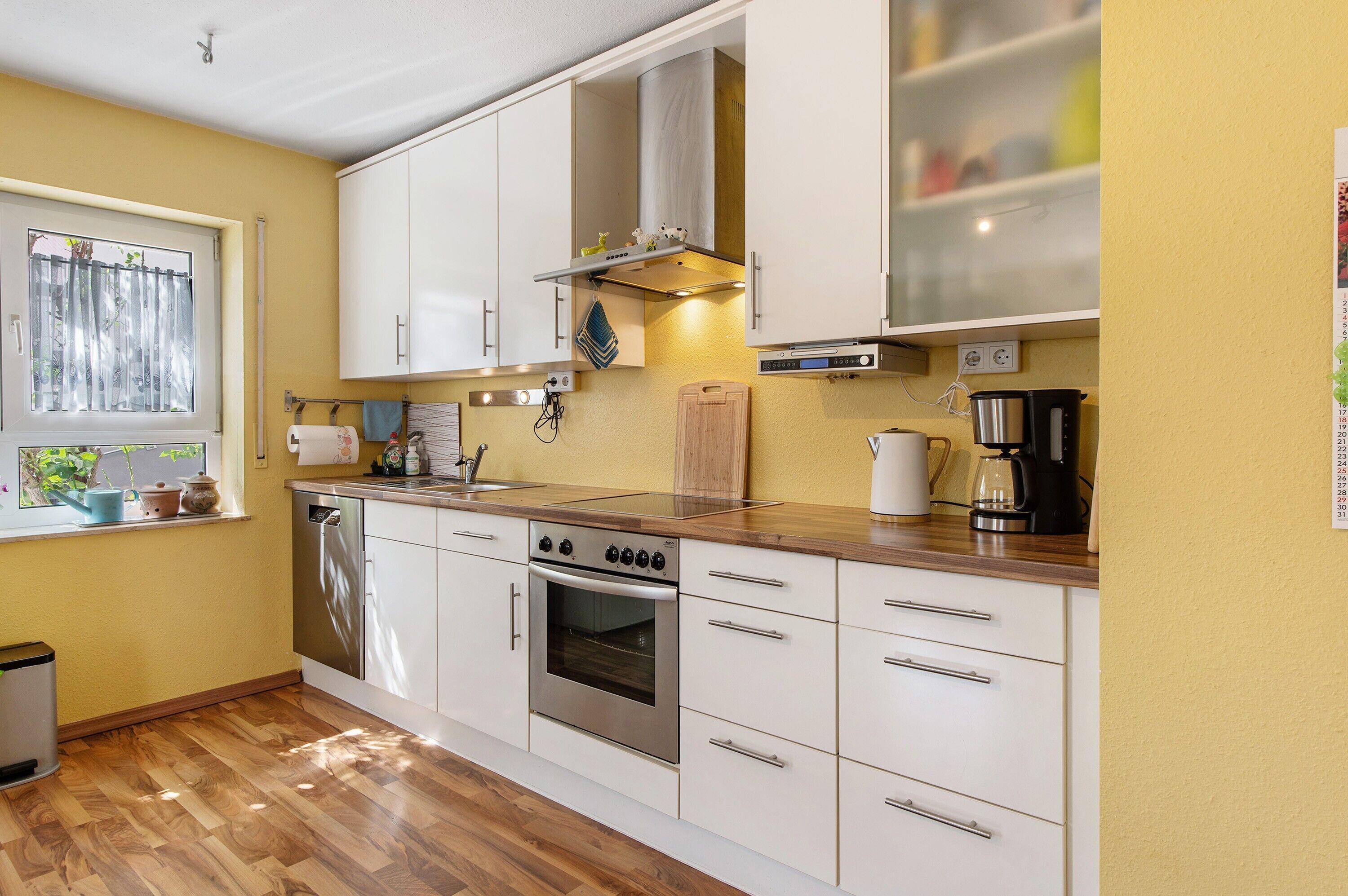 A kitchen with white cabinets, a stainless steel oven, a coffee maker, and a window with plants.