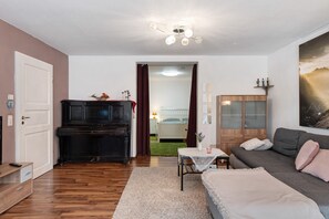 Een woonkamer met een piano, bank, tafel en een kast.
