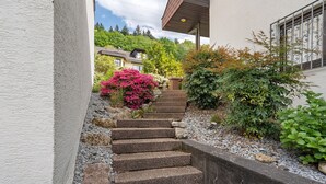 Un escalier en pierre mène à un bâtiment à l’extérieur blanc, entouré de verdure et sous un ciel dégagé.