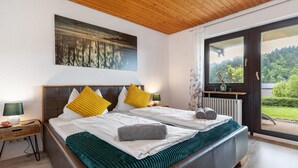 Une chambre avec un grand lit, une table de chevet, une fenêtre donnant sur un paysage verdoyant et un tableau accroché au mur.