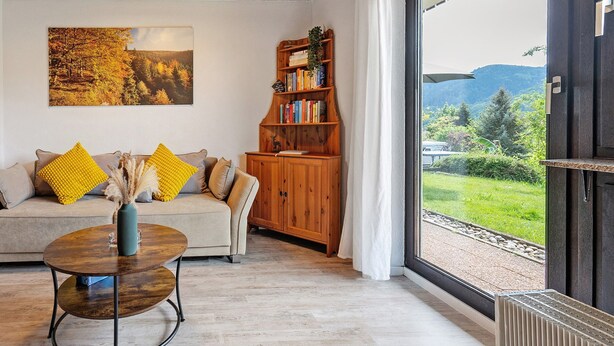 Un salon comprenant un canapé, une table basse, une bibliothèque et une grande fenêtre donnant sur un paysage verdoyant et montagneux.