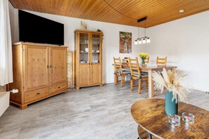 Zona pranzo con tavolo in legno, sedie e televisore montato su un mobile.