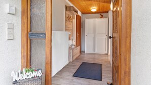Un couloir intérieur en bois, avec une pancarte de bienvenue, un radiateur, une porte et un paillasson sur le sol.
