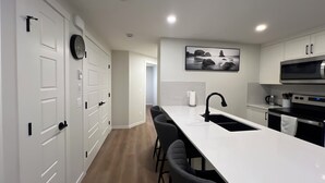 A modern kitchen with a central island, black bar stools, a stainless steel oven, and a microwave. - Cozy 2 bedrooms Suite Near Calgary Airport ✈️ | Air conditioning Sleeps 6 (Calgary)