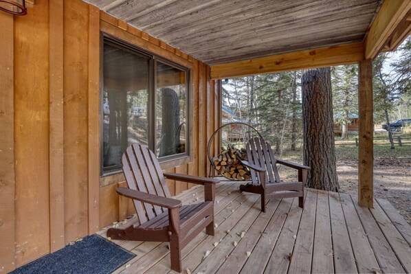 A wooden deck with two Adirondack chairs and a stack of firewood.