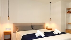 A neatly made bed with a dark blue bedspread and white linens, two bedside tables with wooden finishes, and a hanging light fixture above the bed.
