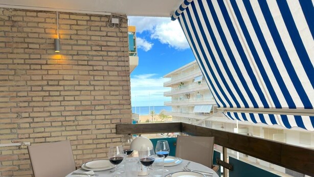 A dining table set for four with plates, glasses, and cutlery, overlooking a beach and a hotel building.