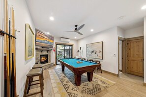 A room with a pool table, a fireplace, and a ceiling fan.