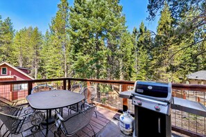 A deck with a grill, table, and chairs, surrounded by trees.