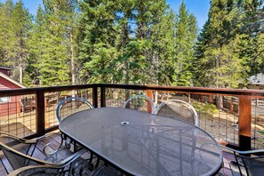 A metal table and chairs on an outdoor deck with a view of tall pine trees.