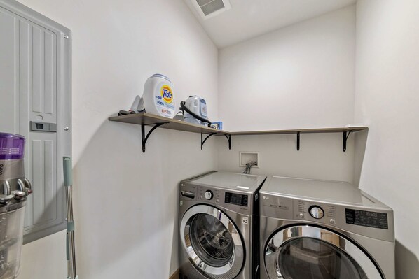 A laundry room with two front-loading washers, a shelf with Tide detergent, and a water heater.