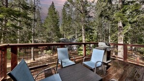 A deck with outdoor seating and a grill, surrounded by tall trees. - Tahoe Forest Lodge: A/C, Hot Tub, Pool Table (South Lake Tahoe)