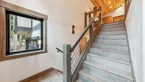 A staircase with a wooden finish, a metal railing, and a window with a view of outdoor trees. - Tahoe Forest Lodge: A/C, Hot Tub, Pool Table (South Lake Tahoe)